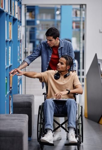 Young man assisting student with disability in library